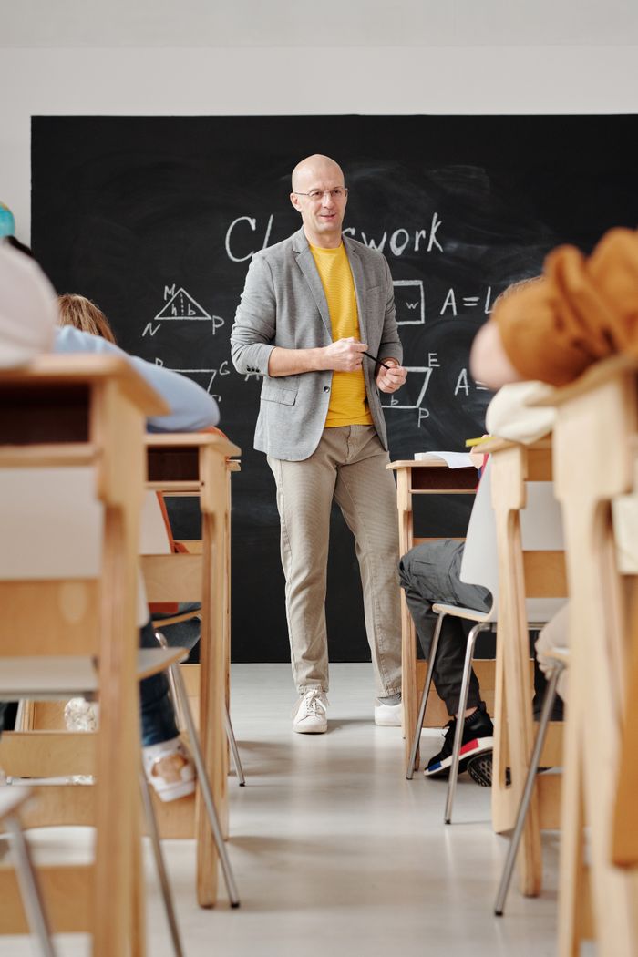 About Bald teacher explaining geometry on blackboard to attentive students in classroom.